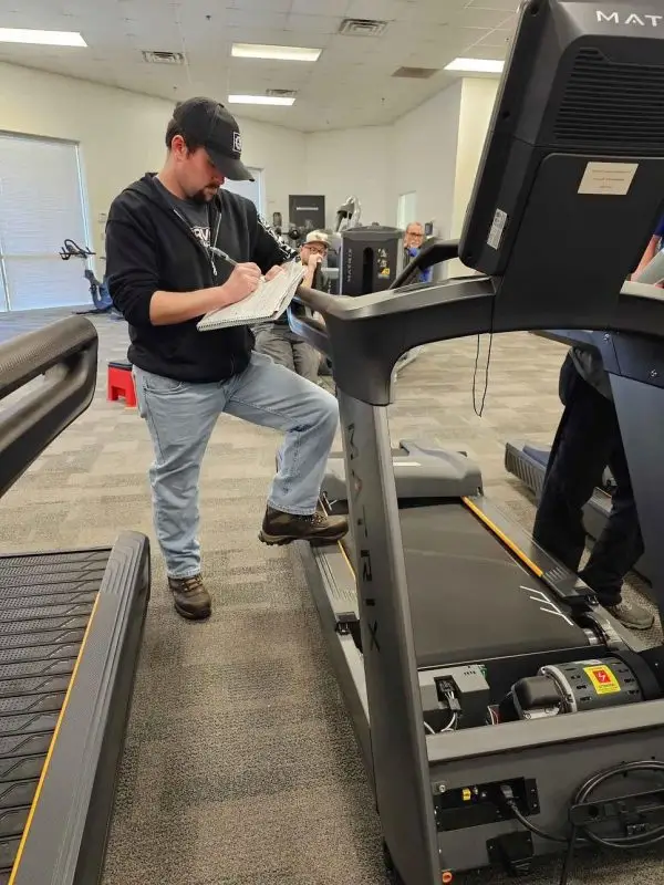 Gym equipment technician inspecting treadmill – Preventive fitness equipment check-up in UAE